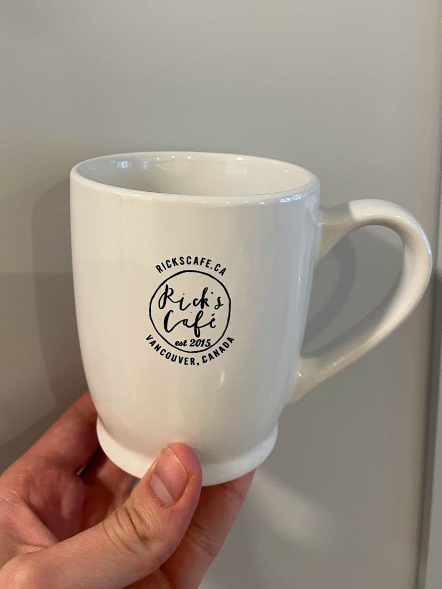 A hand holding a white Rick’s Café mug